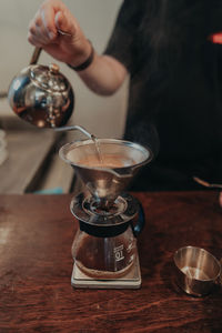 Midsection of woman pouring coffee in cup on table