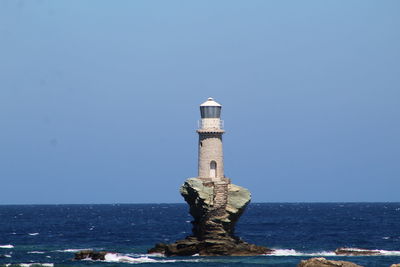 Lighthouse by sea against clear sky