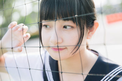 Close-up of thoughtful young woman looking away by net outdoors