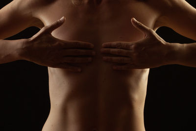 Midsection of shirtless man covering chest against black background
