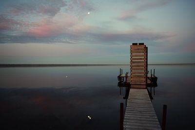 Pier amidst river against cloudy sky at dusk