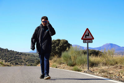 Man standing by road sign against clear blue sky