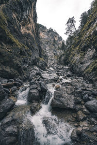 Low angle view of stream amidst rocks against sky
