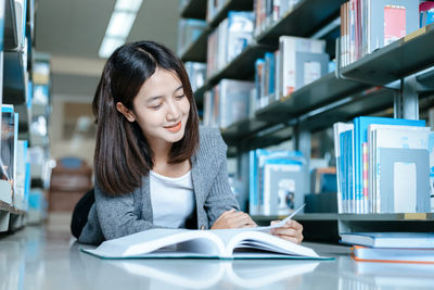 Smiling woman reading book lying on floor in library