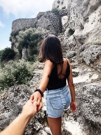 Cropped image of man holding woman hand on rock