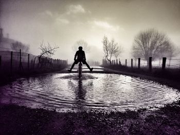 Silhouette boy riding bicycle in water against sky