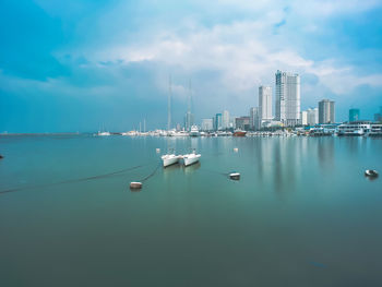 Sailboats in sea by modern buildings against sky