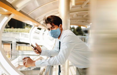 Portrait of man holding smart phone standing on footbridge