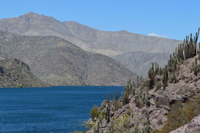 Scenic view of lake and arid mountains against clear blue sky