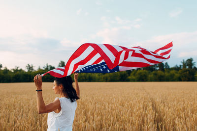 Woman holding umbrella while standing on field against sky