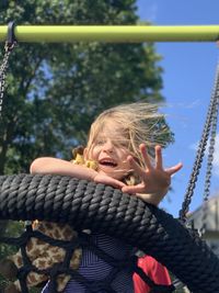 Low angle portrait of cheerful girl lying on swing