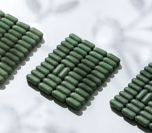 Pattern of pills of chlorella, spirulina, barley in rows on white background with shadow  supplement