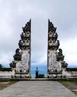 Young woman standing at historic built structure against cloudy sky