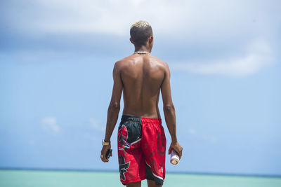 Rear view of shirtless man standing against sea against sky