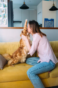 Young woman playing at home with her maine coon cat on the couch