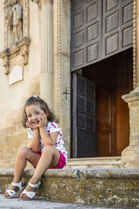 Portrait of smiling girl sitting against building