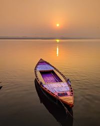 Boat moored in lake against sky during sunset