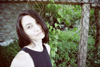 Portrait of beautiful woman standing by chainlink fence