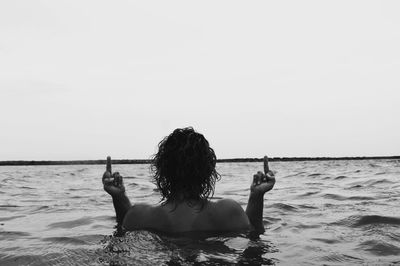 Rear view of woman gesturing while swimming in sea against sky