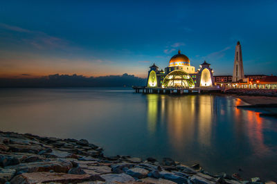Illuminated mosque by sea at sunset