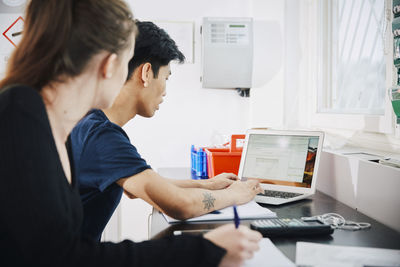 Young woman sitting by man using laptop in classroom at university