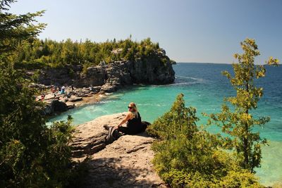 Woman sitting on rock by sea against clear sky