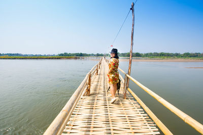 Full length of woman walking on suspension bridge amidst lake against sky