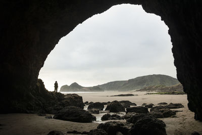 Rear view of man standing rock formations by sea against sky