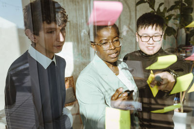 Multiracial male and female colleagues discussing over sticky notes in creative office