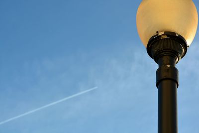 Low angle view of street light against sky with airplane chemtrail