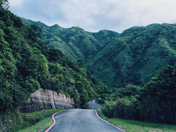 Road amidst trees and mountains against sky