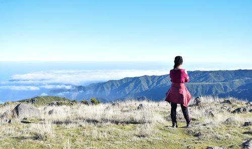Rear view of woman standing on grass against mountain and sky