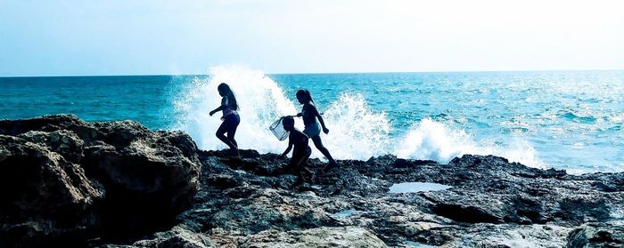 People on rocks at sea against clear sky