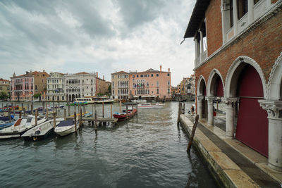 Boats moored in canal amidst buildings in city against sky