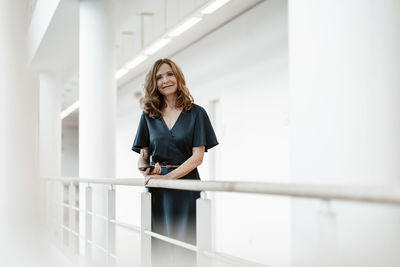 Portrait of young woman standing against railing