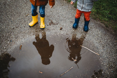 View from above reflection of young kids on puddle wearing rain boots