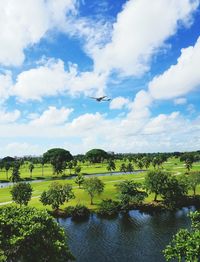 Airplane flying over field against cloudy sky