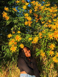 Beautiful young woman standing by yellow flowering plants