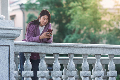 Full length of man using mobile phone while sitting on railing