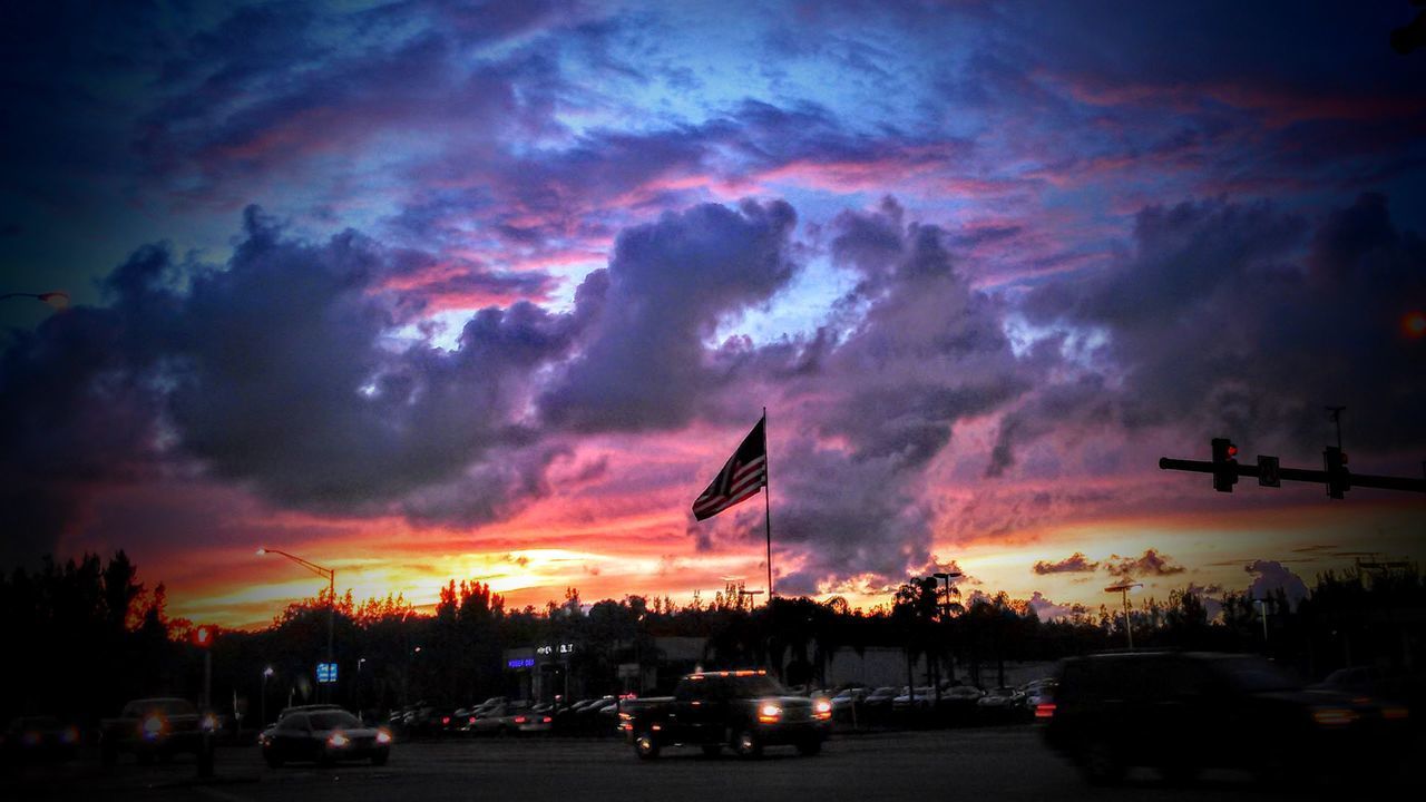 CARS ON CITY STREET AGAINST DRAMATIC SKY