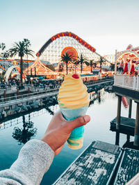 Person holding ice cream in amusement park against sky