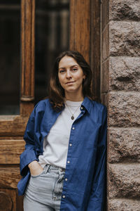 Portrait of non-binary person with hand in pocket leaning on wall