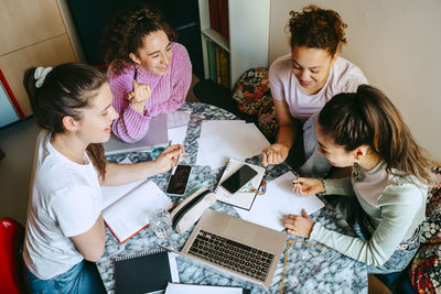 High angle view of female friends discussing while studying together at home