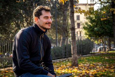 The young man is sitting on the bench in the park in rome. 