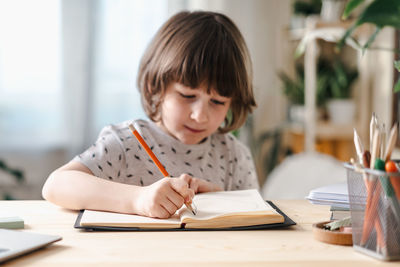 Distance learning online education.  smile kid boy studying at home with laptop, writing in notepad 