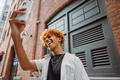 Young dark-skinned man posing at the street and taking selfie in the city background