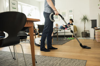 Low section of father cleaning floor with vacuum cleaner at home