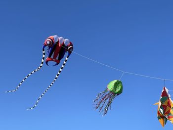 Low angle view of kites flying against clear blue sky