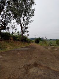 Empty road amidst trees on field against sky