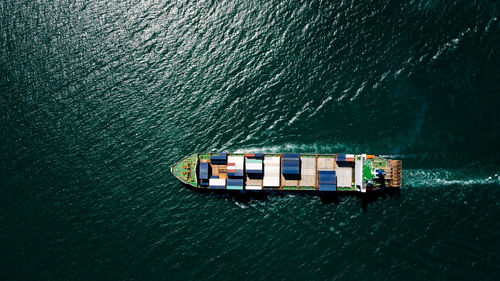 Aerial top view container ship sailing on the green sea full speed container for logistics, 